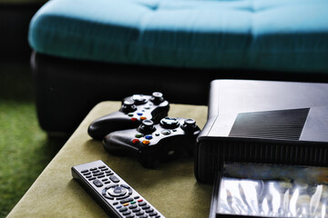 Close-up of remote control, game console and disc packaging on table in living room