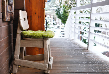 Terrace of a wooden house overlooking the winter forest. On the terrace there is a wooden chair with a green cushion