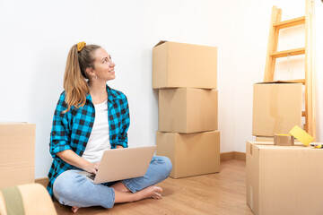 Portrait young happy woman sitting on the floor with many boxes, working with computer in a new house. - Caucasian beautiful girl - High quality photo