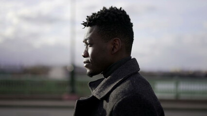 Thoughtful profile black man portrait walking outdoors in city wearing coat