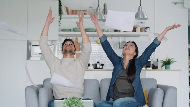 Video of happy couple tossing invoices and documents into the air while sitting on the couch at home.