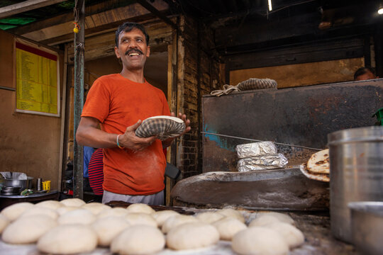 Cook of a local roadside restaurant or a dhaba,  making bread or a roti, in a clay wood fired oven or a  tandoor  