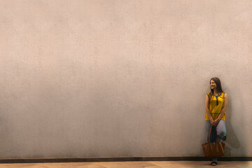 Long distance shot of an Indian woman with bag standing against wall