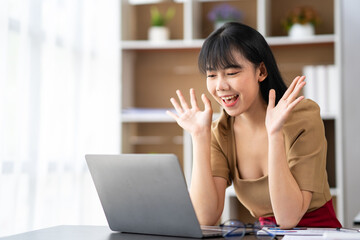 happy asian businesswoman waving hand while sitting on couch and having video chat on laptop