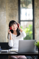 Happy Asian woman relaxing and listening to music in office with computer laptop and coffee cup. People and lifestyles concept. Freelance and outdoors workplace outdoors theme.