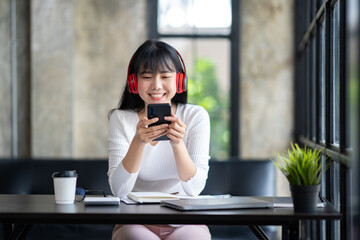 Young adult happy smiling Asian student wearing headphones talking in online chat meetings using a laptop on a university campus or at a virtual office. College female students learning remotely.