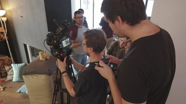 Over-shoulder of female and male movie production crew members watching shooting process in house setup