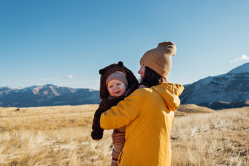 mother holds a child in her arms in the mountains against the background of yellow grass in autumn