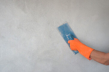 worker hand with glove holding trowel is plastering cement wall