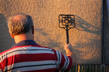 Balding man cleans a carpet outdoors at summer evening in sunset.