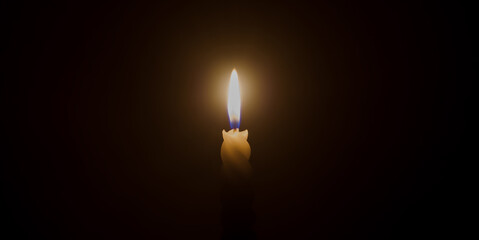 A single burning candle flame or light glowing on a spiral white candle on black or dark background on table in church for Christmas, funeral or memorial service