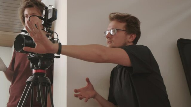 Medium side-view of male Caucasian movie director talking to videographer and invisible actors on stage behind camera