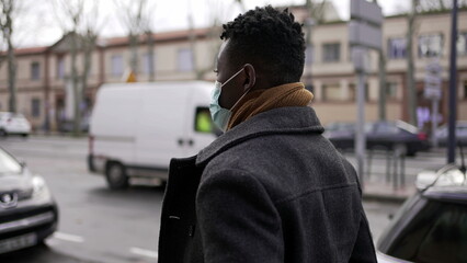 Young black man wearing covid-19 face mask walking in city downtown during pandemic, tracking shot