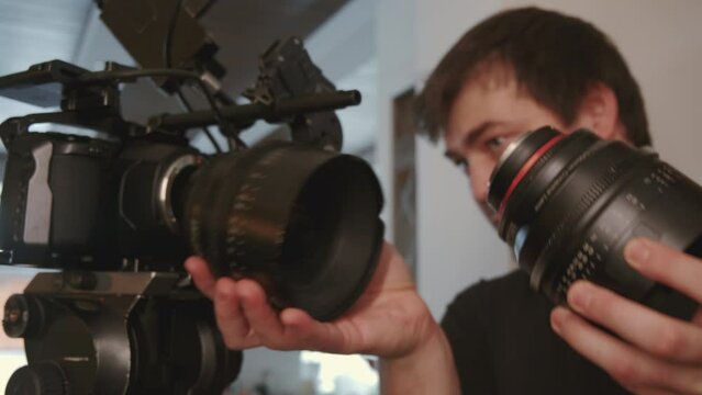 Low angle close-up of male videographer changing lenses on movie camera on shooting set indoors at daytime
