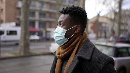 Fototapeta na wymiar Young black man wearing covid-19 face mask walking in city downtown during pandemic, tracking shot