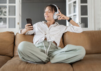 Obraz premium Enjoys music in the app during a break at home. The woman uses Bluetooth headphones.