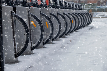 Row of many parked rental bicycles wheels, winter snow storm day scene. Urban transportation...