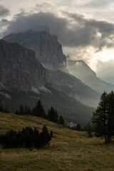 Bright cloudy sky over steep rocky mountains and green valley in Dolomites, Italy