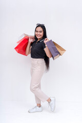A young lady in a dark top and khaki pants holding shopping bags on both hands after going on a shopping spree. Isolated on a white background. Retail and sale concepts.