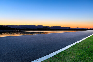 Asphalt road and lake with mountain nature background at sunset