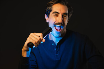 Glad singer with neon light in hand in dark room