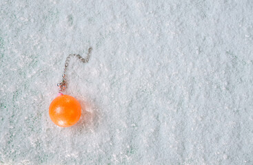 orange decorative christmas bubble with decorative chain lying on white snow, top view