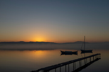 Obraz premium View of boats and pier on sunset sunrise or midday with reflection on water and sun light with cloudy sky