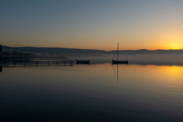 View of boats and pier on sunset sunrise or midday with reflection on water and sun light with cloudy sky