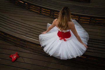 Young ballerina wearing red and white christmas dress sitting. Pointe shoes  on floor.  Ballet...