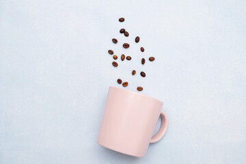 Obraz na płótnie Canvas Pink mug with falling coffee beans on a blue background. There is space for text.Abstract image of a mug with coffee.