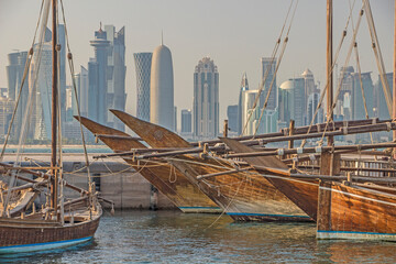 Qatar - Doha - Traditional wooden dhow boats moored at Dhow harbor in contrast with West Bay skyscrapers skyline on background - obrazy, fototapety, plakaty