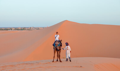 A woman riding a camel across the thin sand dunes of the in Western Sahara Desert, Morocco, Africa