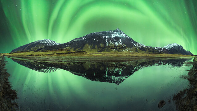 Calm water of lake washing embankment with snowy mountains under polar lights