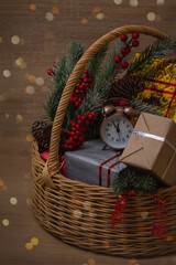 Wicker basket with gifts and spruce branches. On one of the gifts there is an alarm clock, the arrows of which show 23.55. Wooden background, the photo is decorated with beautiful gold bokeh, gold, si