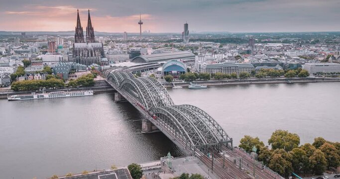 Koln Aerial video timelapse with trains move on a bridge over the Rhine River on which cargo barges and passenger ships ply. The majestic Cologne Cathedral in the background