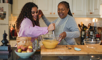 Happy african mother and daughter dancing together to music playlist while baking inside ktichen at...