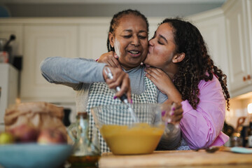 Fototapeta na wymiar Happy african daughter kissing her mother while baking together inside kitchen at home