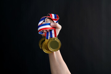 Human hand holding gold medals on black background