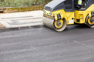 Naklejka premium Road roller and asphalt paver machine at the construction site, with hot concrete and smoke
