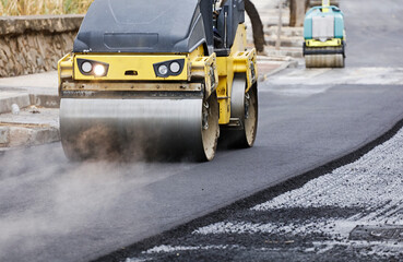 Road roller and asphalt paver machine at the construction site, with hot concrete and smoke