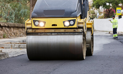 Road roller and asphalt paver machine at the construction site, with hot concrete and smoke