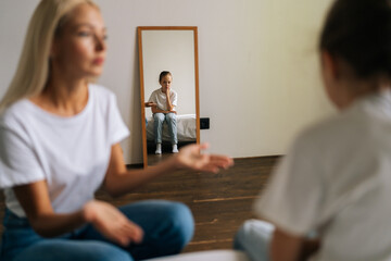 Reflection in mirror detached sad little girl during stressed mother scolding, shouting and...