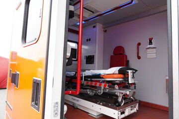 View through open side door of the orange ambulance car. Inside are movable stretcher and other medical equipment.