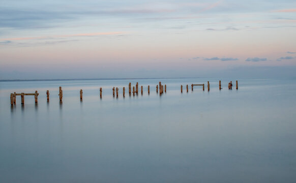 A clear November evening long exposure looking across the old weathered pier posts at Swanage with a pink sky © Kenn