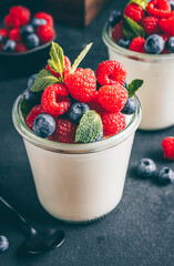 Homemade italian dessert panna cotta with fresh raspberry, blueberries and mint in jar on black background
