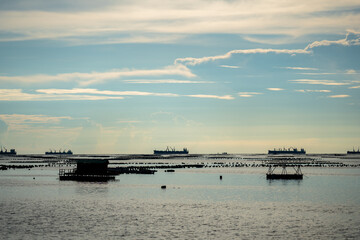 Obraz premium Local fishing boat and container ship are floating on the sea in clear sky day, Sriracha, Chonburi province.