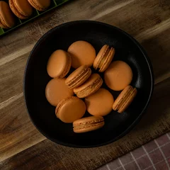Zelfklevend Fotobehang Top view of a bowl of orange-colored French macarons in a black bowl © Pjm Captures/Wirestock Creators