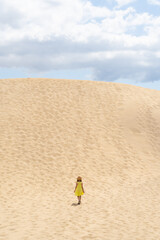 Girl in a yellow dress in the middle of a mountain of sand in a desert
