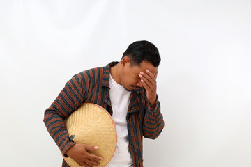 Stressed asian farmer standing while covering his face. Isolated on white background