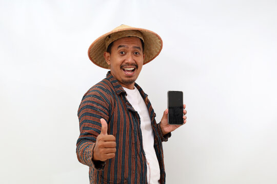 Happy asian farmer standing while showing blank cell phone screen and thumbs up. Isolated on white background